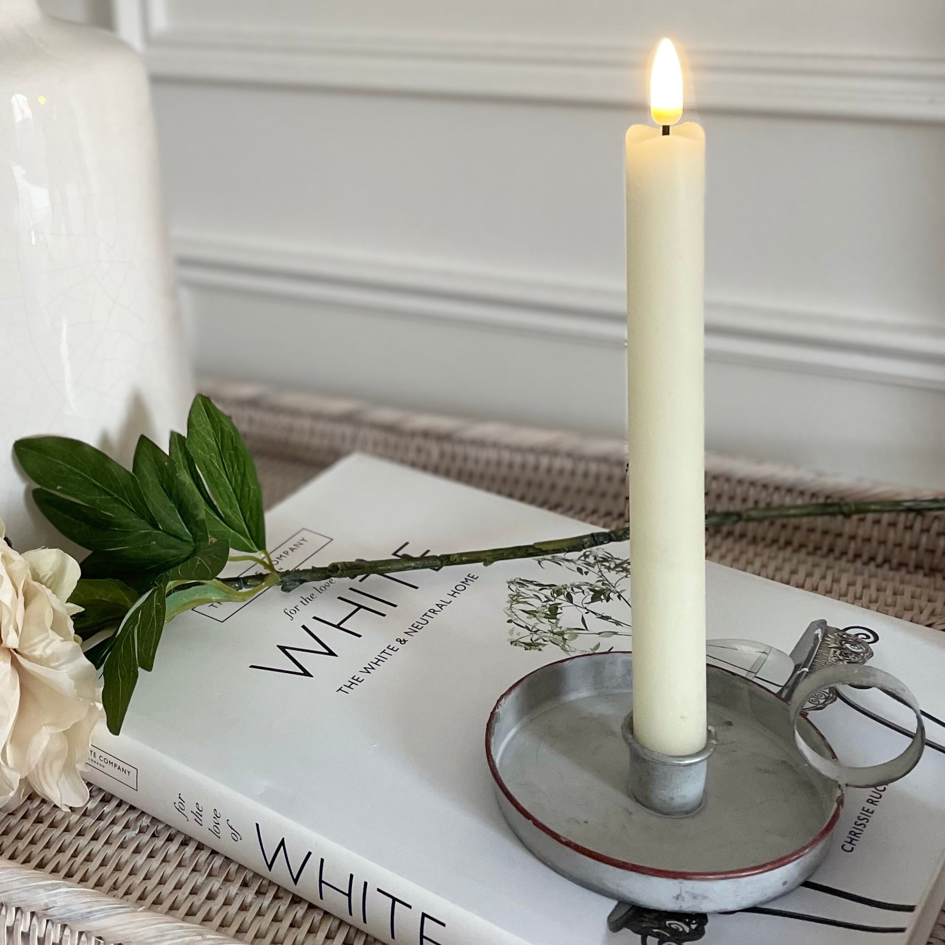 LED dinner candle with realistic flickering flame, 24 cm tall. Placed in a wee willie winkie candle holder, styled on a book.