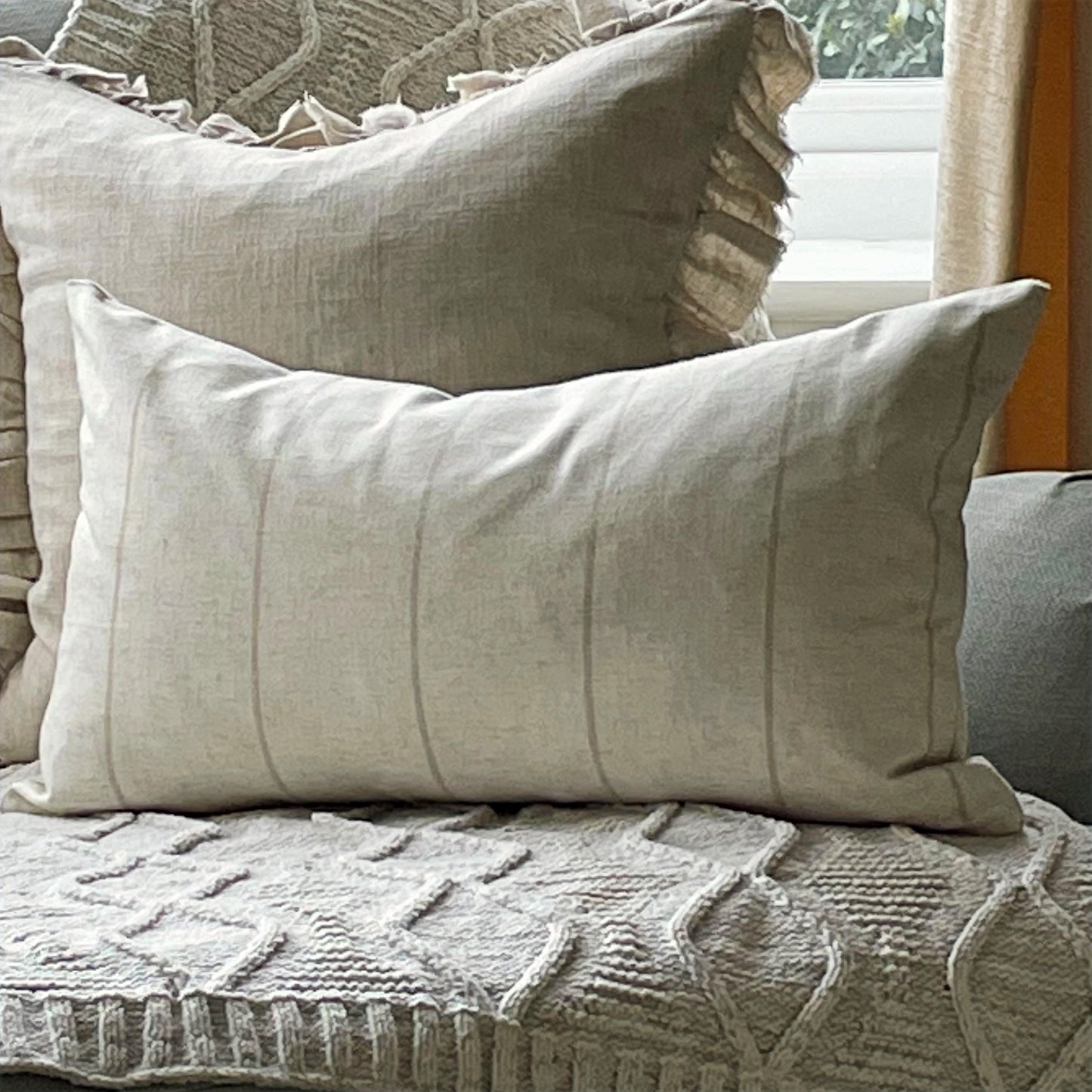 Natural linen blend cushion with thin beige stripes, styled on a neutral sofa for a relaxed country feel.