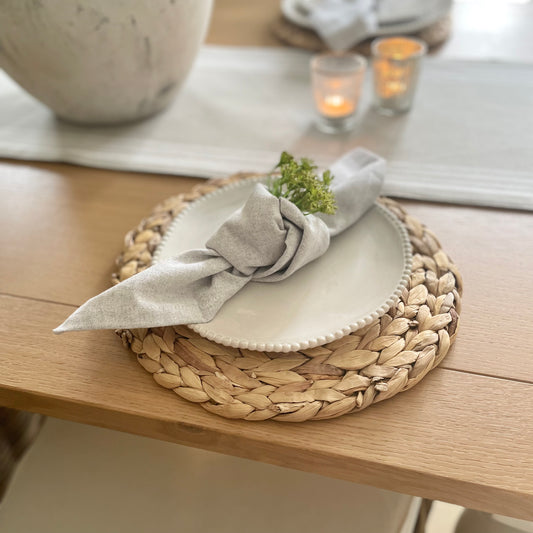 White porcelain side plate with organic shape and beaded detailing around the rim, styled on a wooden dining table with grey runner.
