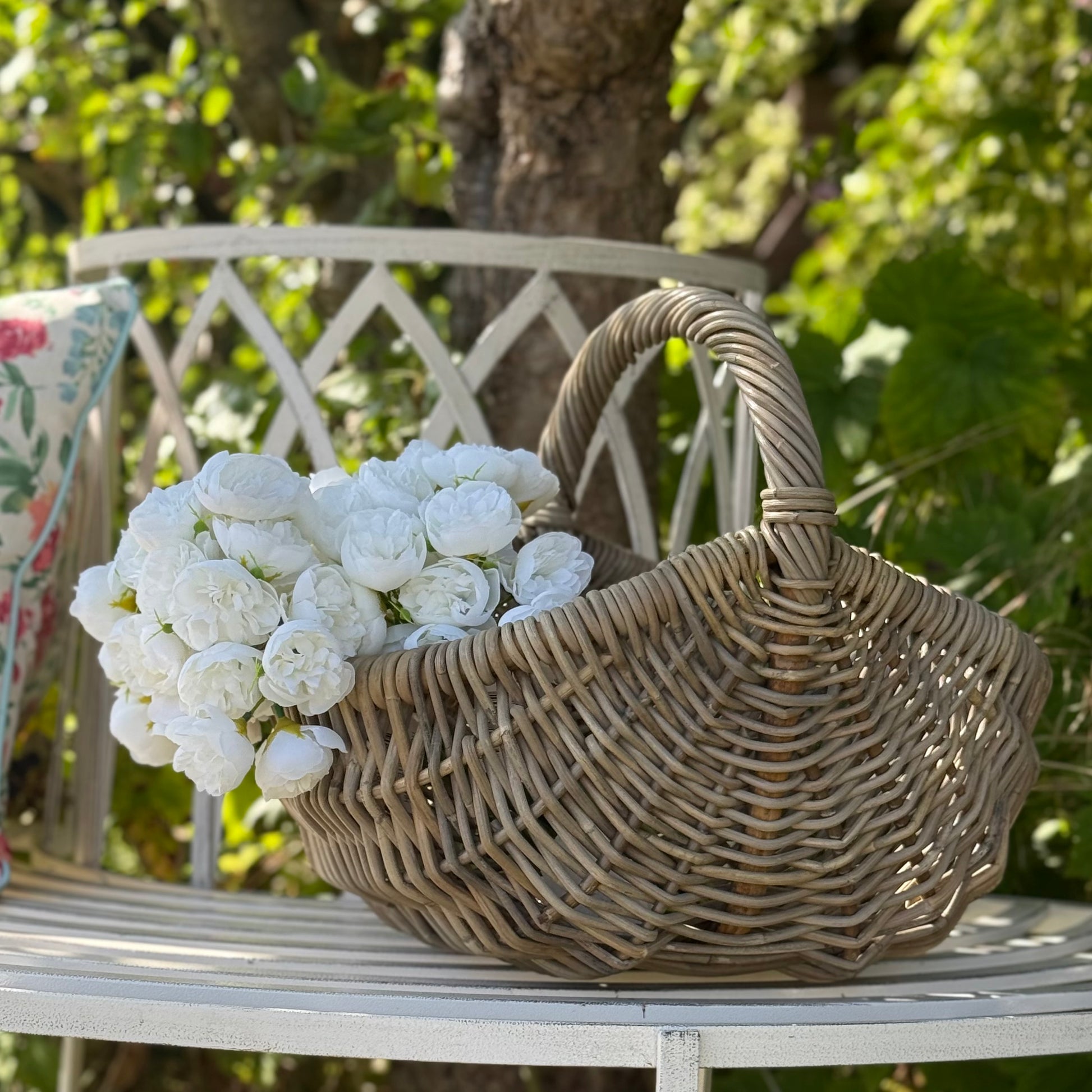 Wicker basket with white flowers on a country bench. 
Handwoven rattan basket with circular handle, perfect for flowers, kindling or home storage