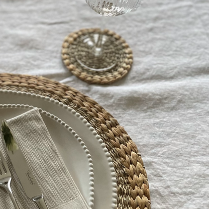 Close up of woven seagrass and water hyacinth texture coasters. Styled on a white linen tablecloth.