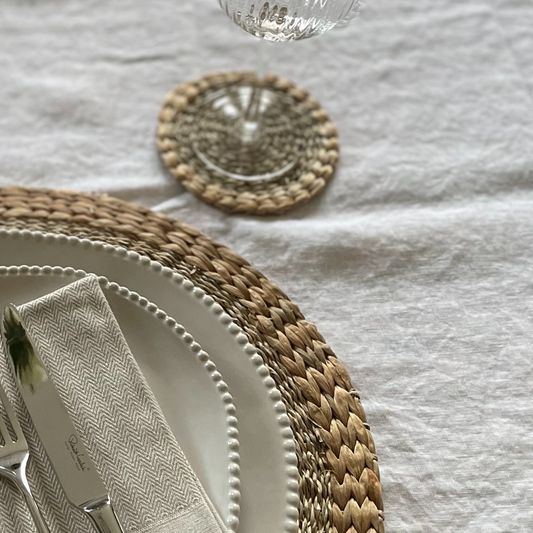 Close up of woven seagrass and water hyacinth texture coasters. Styled on a white linen tablecloth.