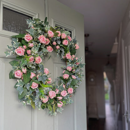 Summer faux wreath with pink roses, ivy and eucalyptus foliage styled on a rustic cottage door.