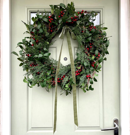 60cm faux winter wreath with fir leaves, red berries and green velvet bow. Styled on a light green front door.