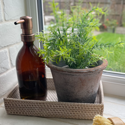 Amber glass refillable bottle with brass effect pump, styled on a kitchen windowsill in rattan tray.