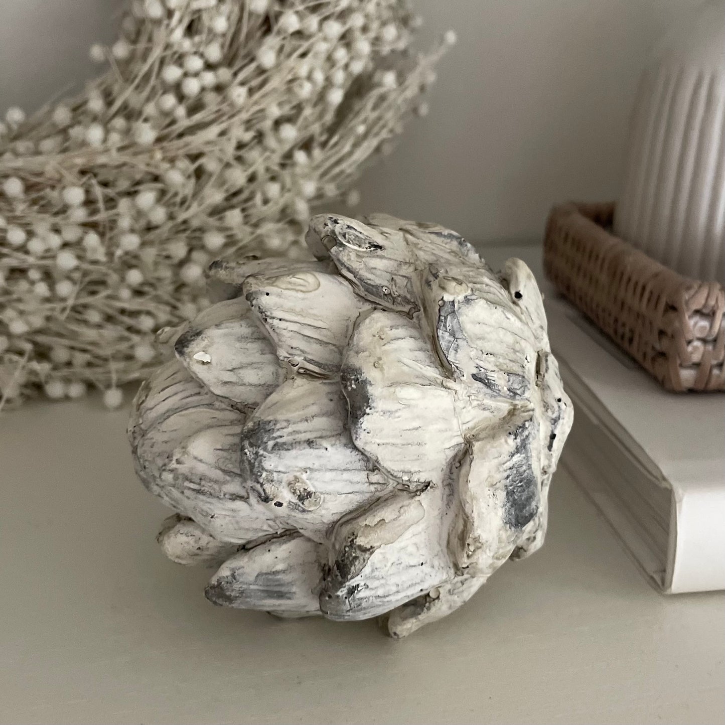 Antique white stone effect artichoke, styled on a shelf with decorative accessories.