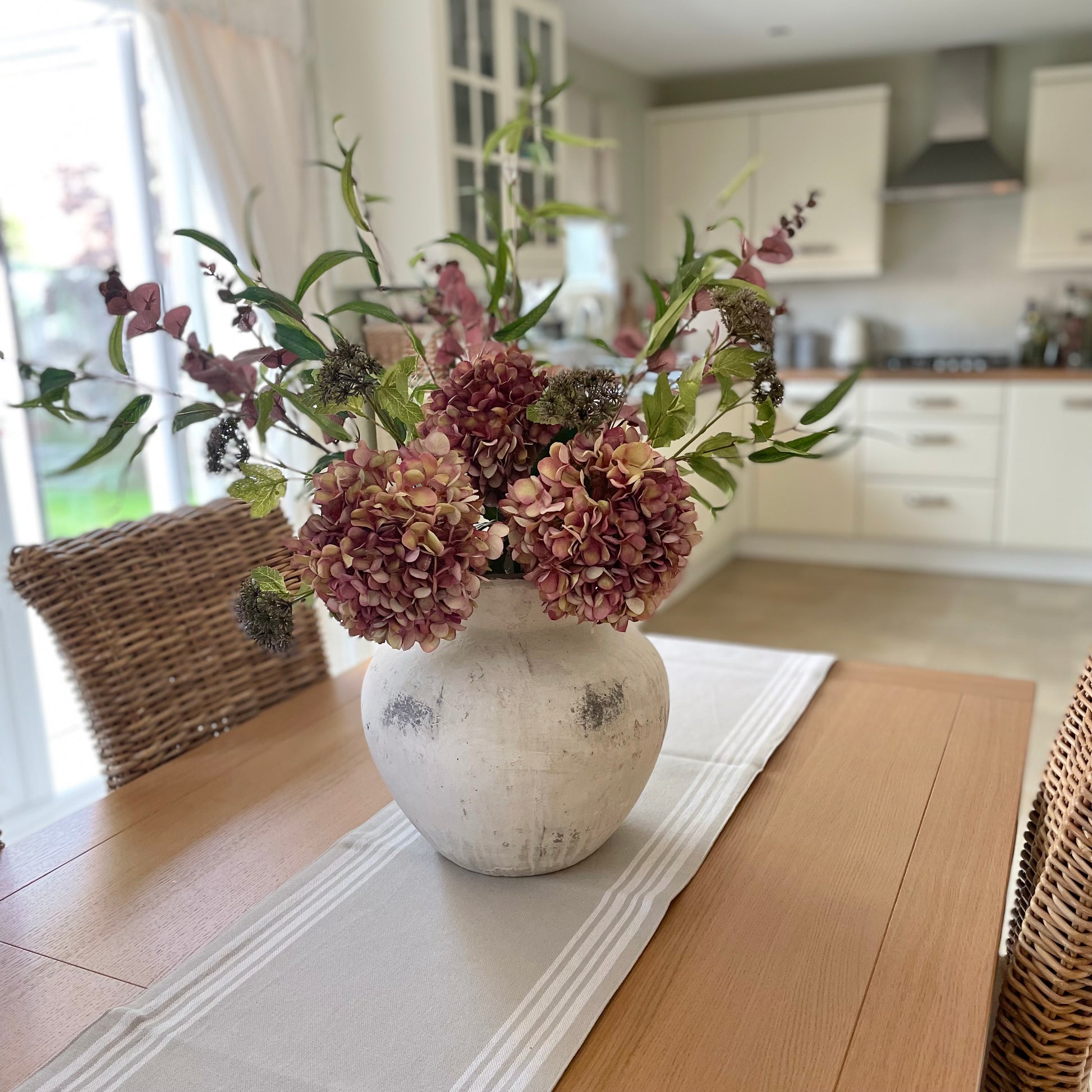 Autumn faux bouquet styled on a wooden dining table in a kitchen setting.