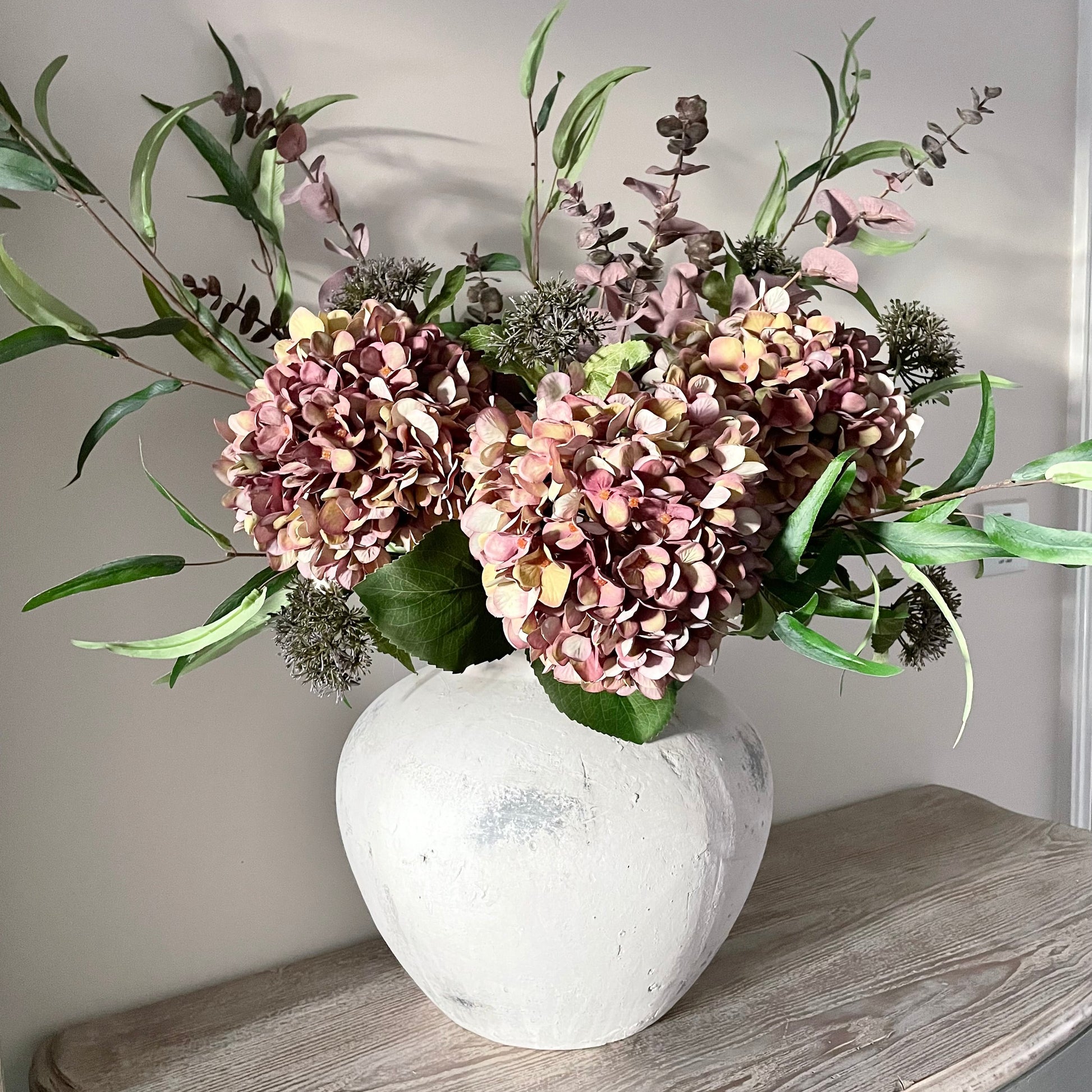 Autumn bouquet of faux flowers in a stone vase on a wooden console table with a neutral background.
