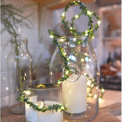 Battery powered 3m LED fairy lights with warm white bulbs and delicate faux foliage, styled along a mantlepiece in a cosy living space.