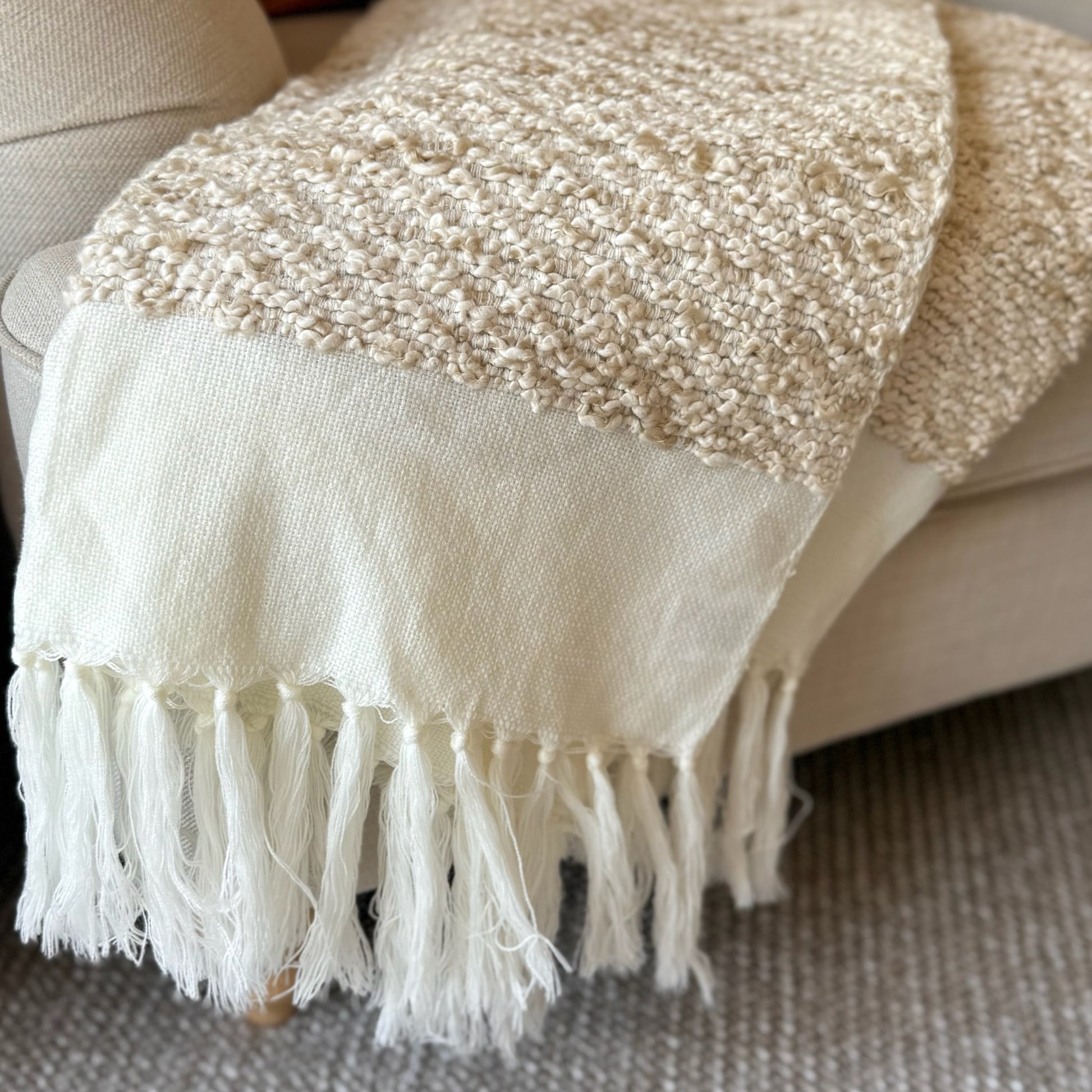 Beige and white textured throw blanket with fringes on a sofa.