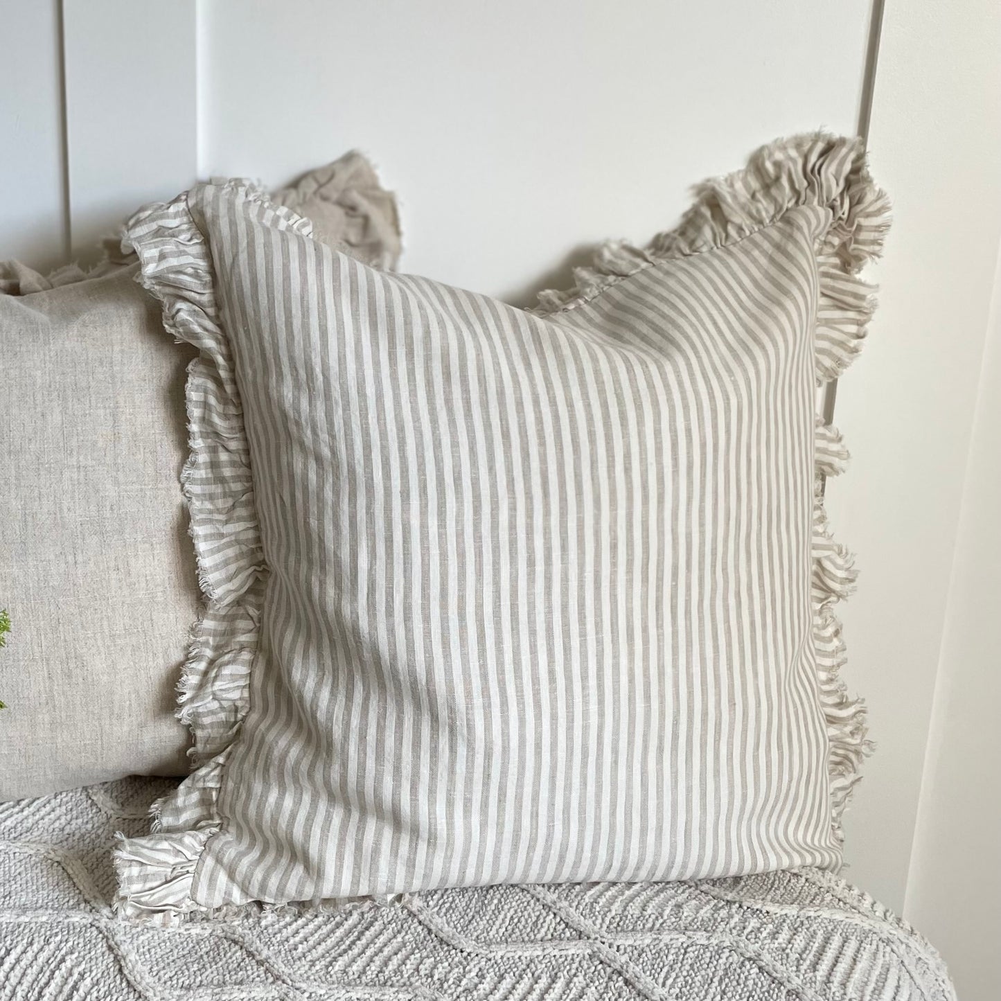 Beige striped ruffle cushion styled on a neutral sofa with soft layered textiles.