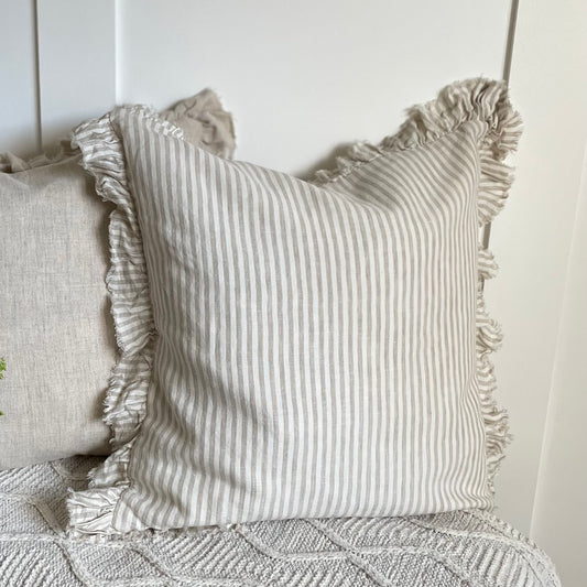 Beige striped ruffle cushion styled on a neutral sofa with soft layered textiles.