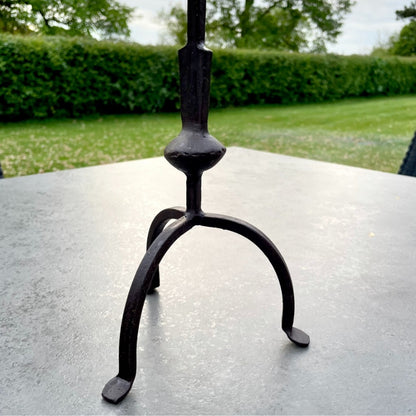 Tall rustic metal candlestick with thin stem and three leg base, styled on a dining table.
