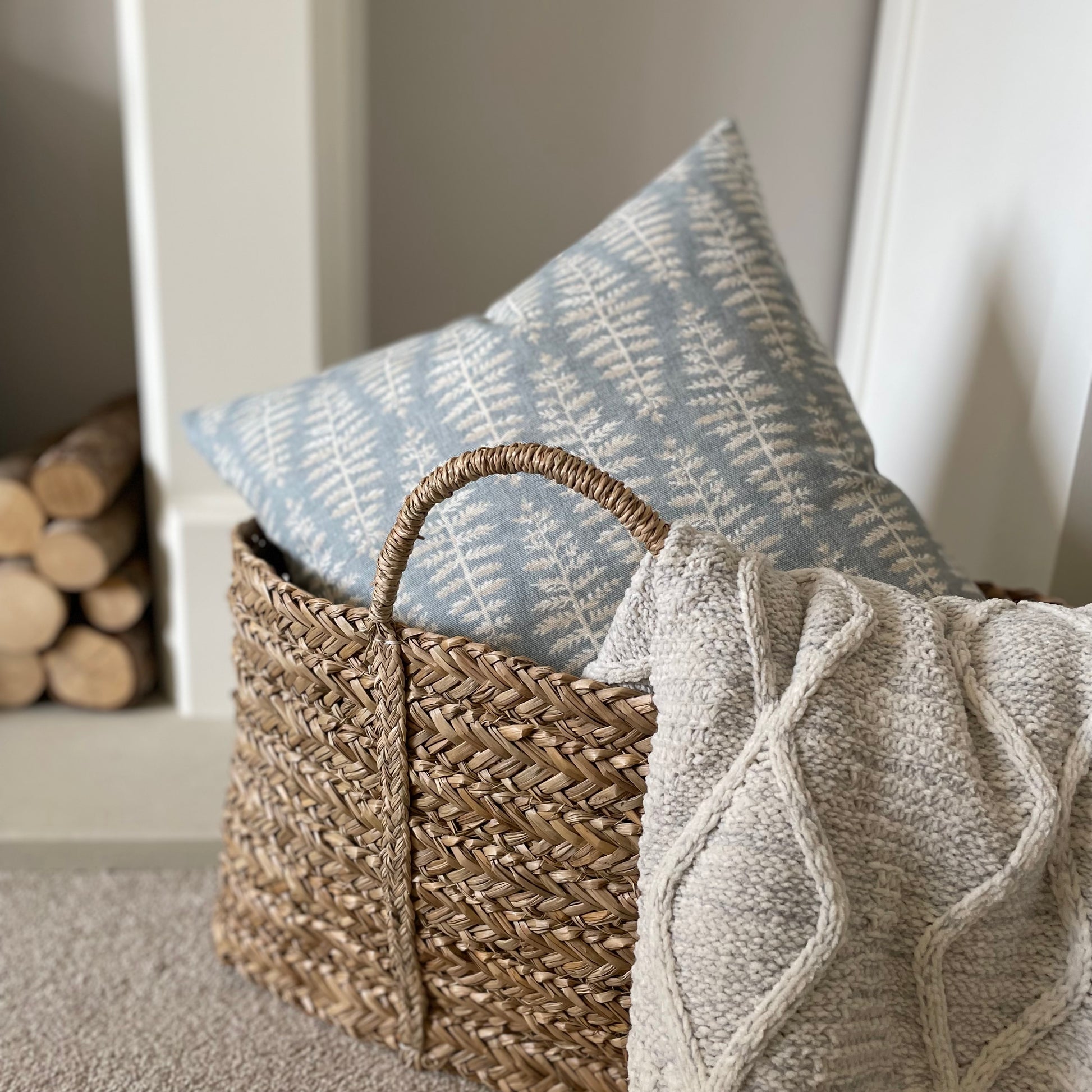 Blue cushion with beige and white leaf print styled on a neutral armchair with a throw.