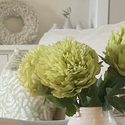 Close up of bright green peony bloom and lush foliage in a white ceramic vase.