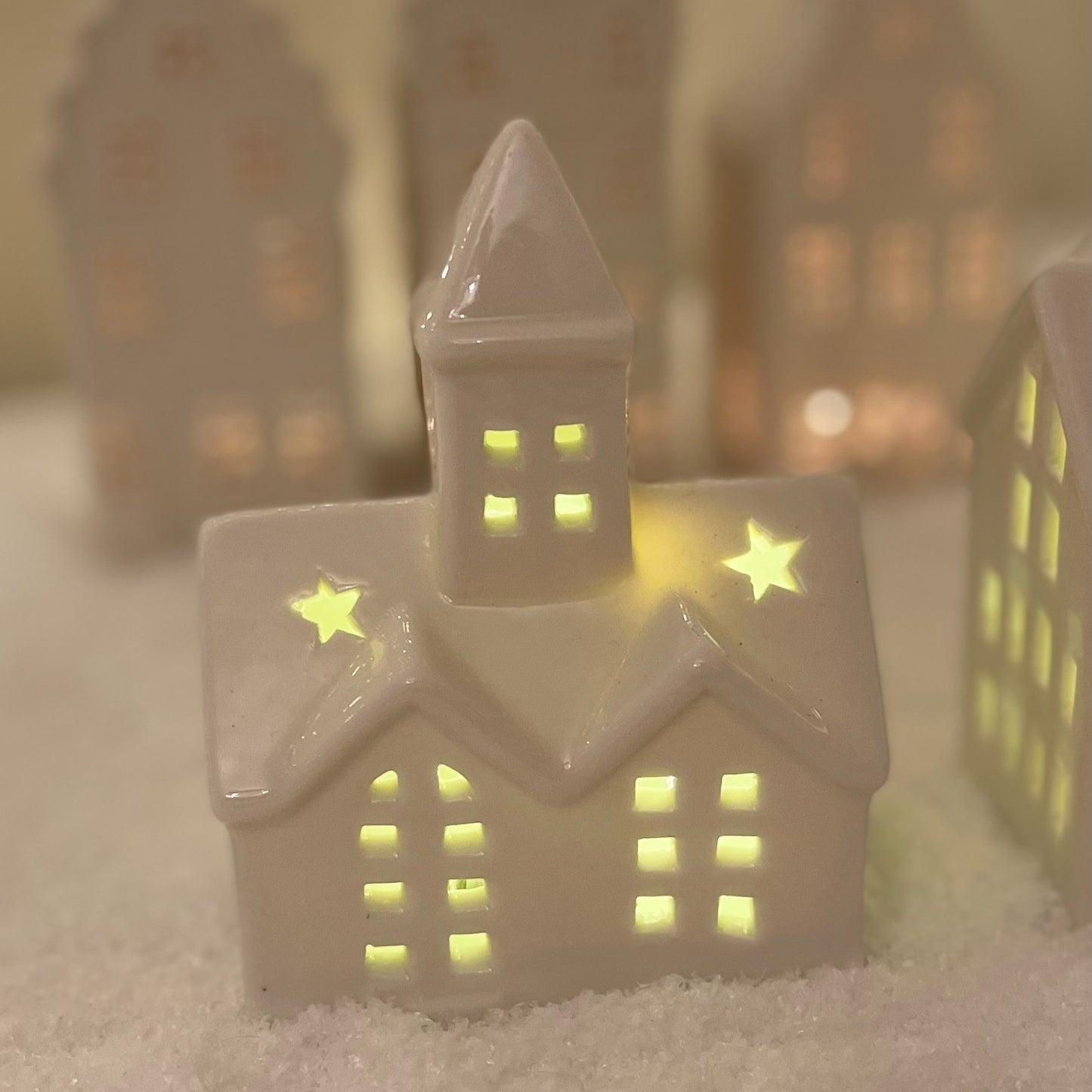 Small white ceramic church ornament with pointed steeple and warm LED light, styled on a festive snow covered mantel.