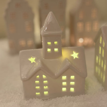 Small white ceramic church ornament with pointed steeple and warm LED light, styled on a festive snow covered mantel.