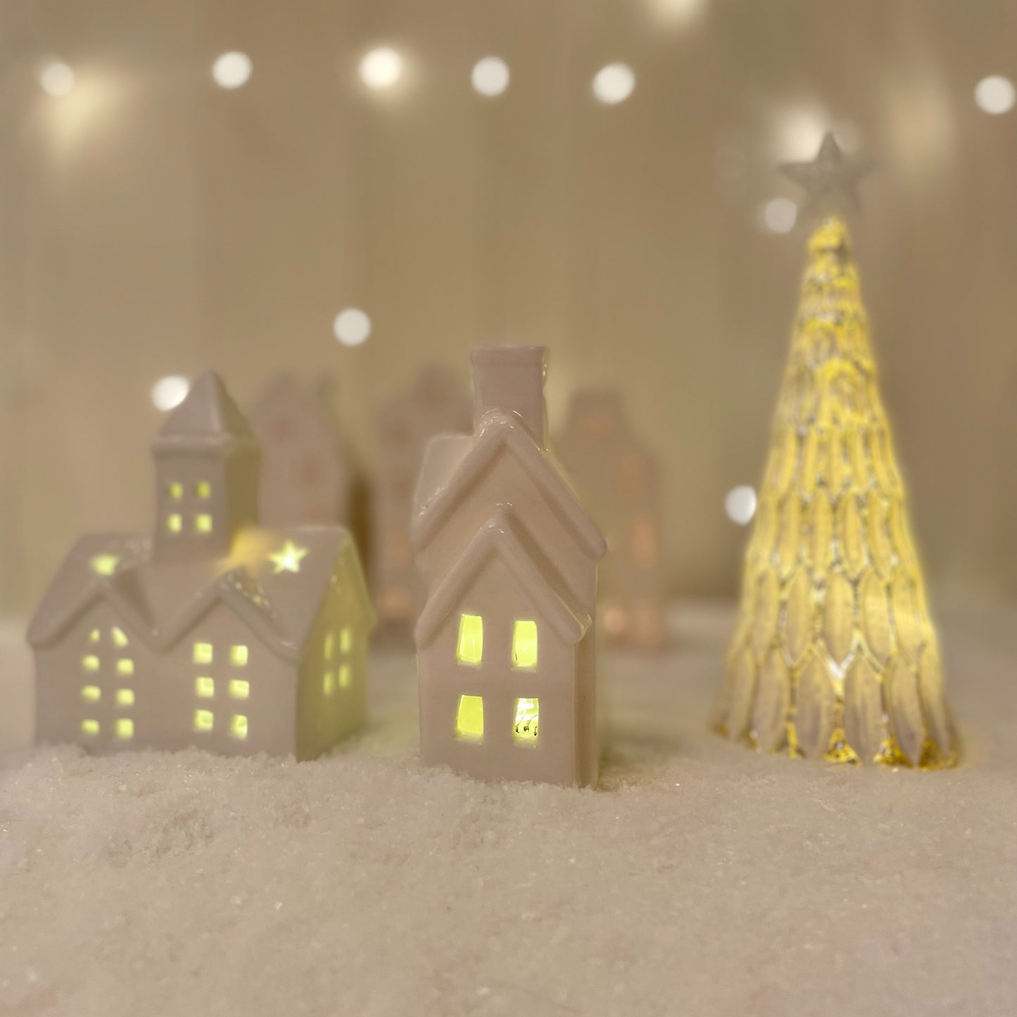 Small white ceramic church ornament with pointed steeple and warm LED light, styled on a snow scene with other christmas ceramic decor.