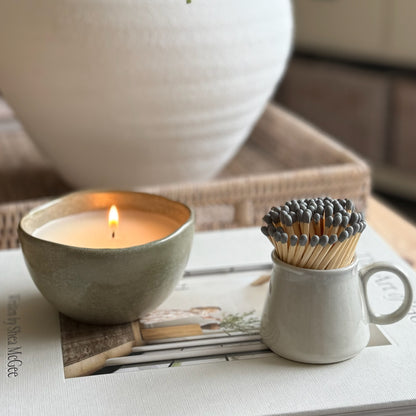 Hand finished grey ceramic espresso style match striker filled with strike-anywhere matches, styled on a neutral coffee table.