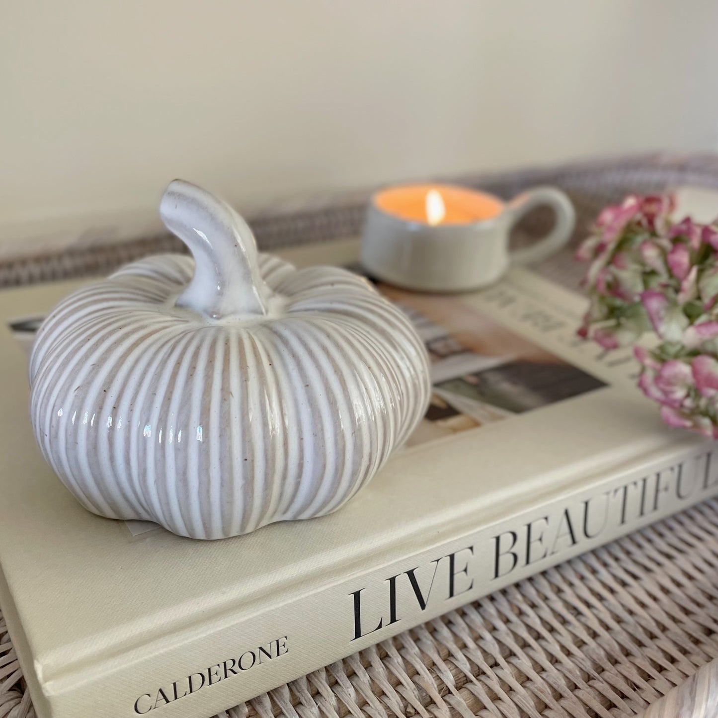 Ceramic squat pumpkin decor, styled on a book with a candle.