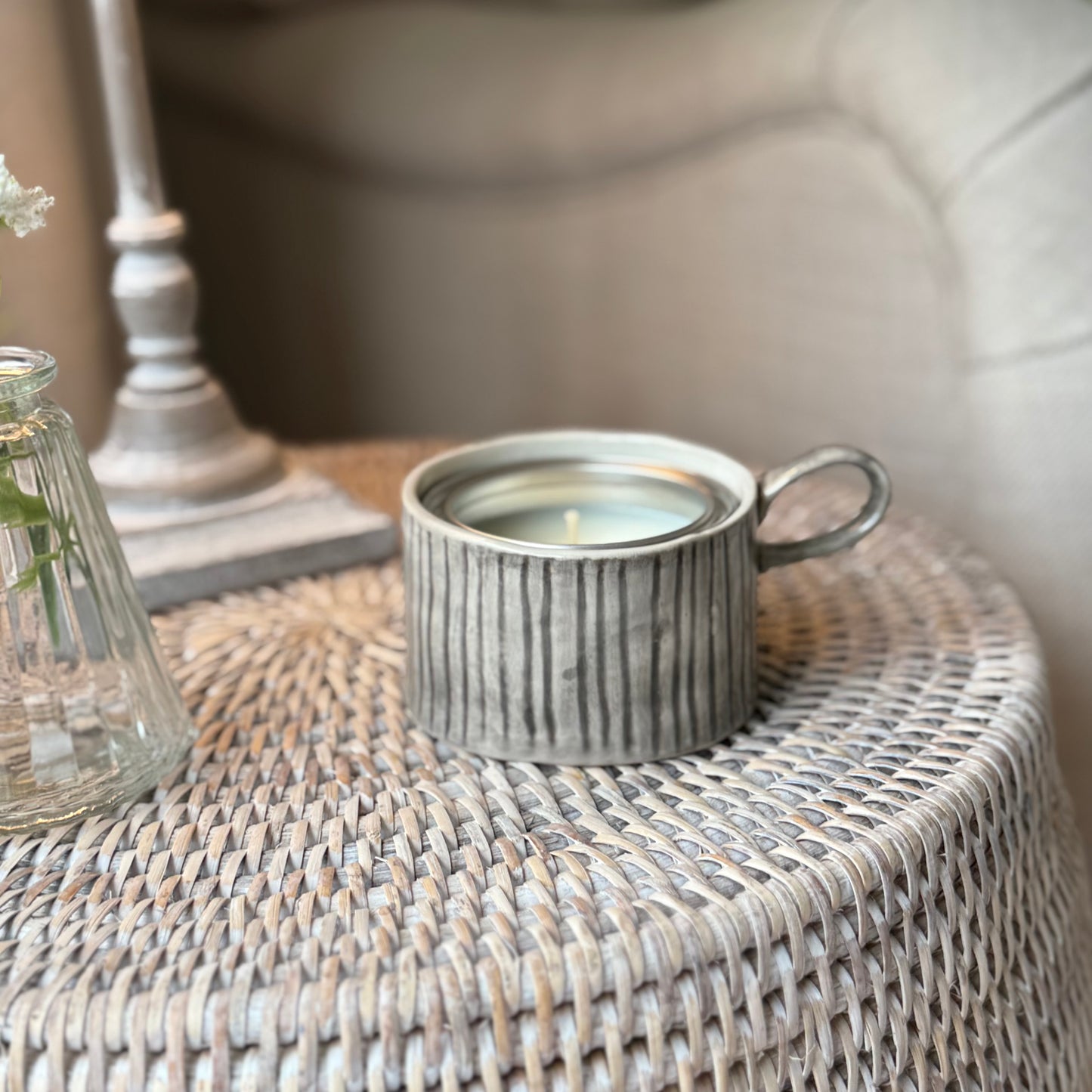 Decorative mug style candle holder on a rattan side table.