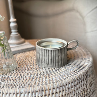 Decorative mug style candle holder on a rattan side table.