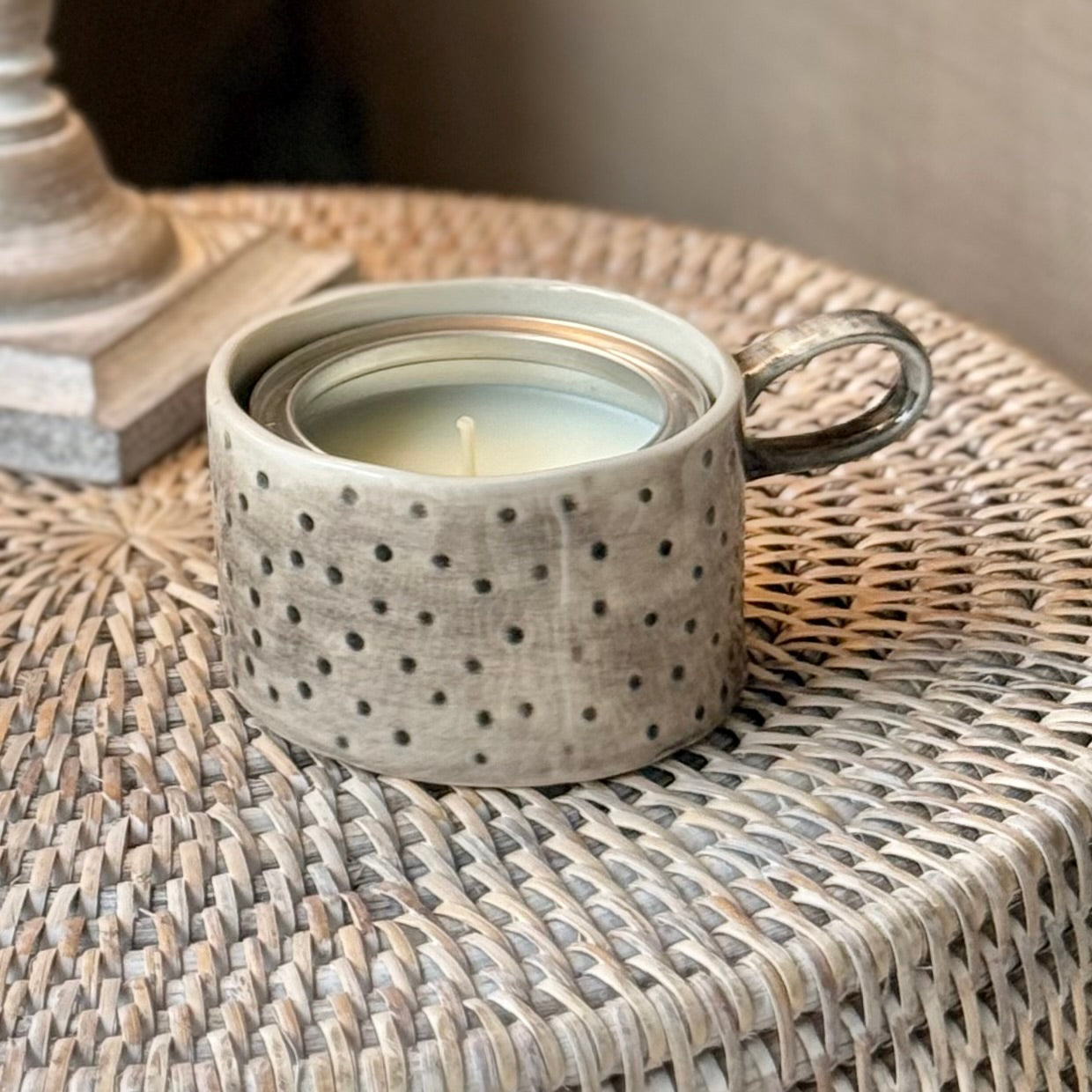 Handmade rustic ceramic mug candle holder in washed taupe with spotted texture and loop handle, styled with candle inside.