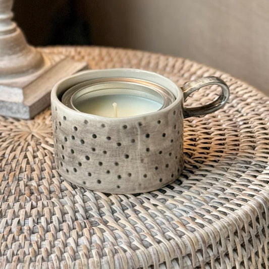 Handmade rustic ceramic mug candle holder in washed taupe with spotted texture and loop handle, styled with candle inside.
