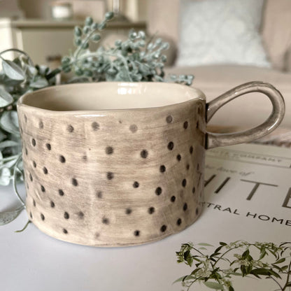 Ceramic mug with decorative spot pattern on a surface with greenery, styled on a book .