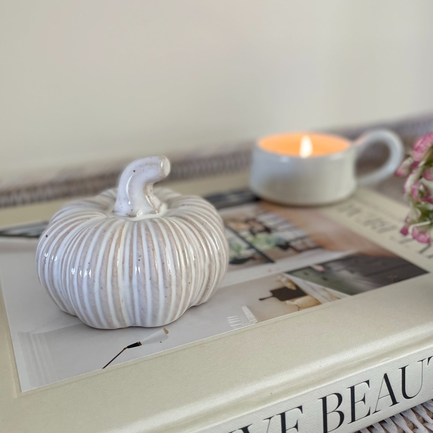 Ceramic squat pumpkin decor, styled on a book with a candle.
