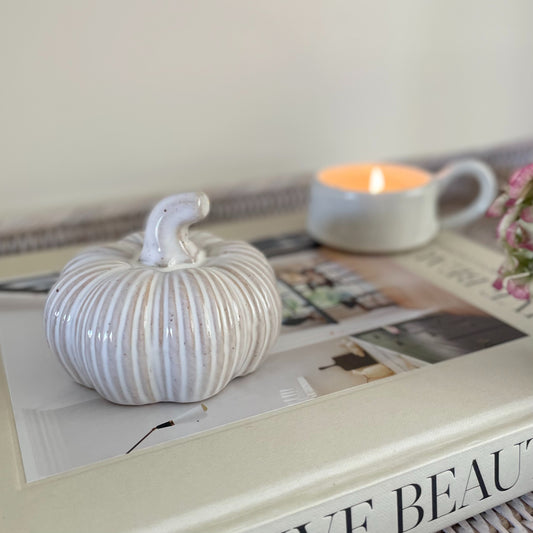 Ceramic squat pumpkin decor, styled on a book with a candle.