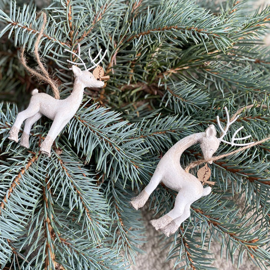 Two ivory resin reindeer with subtle sparkle and a small companion bird, styled on a Christmas tree branch.