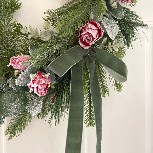 Handmade faux Christmas wreath with frosted red roses, flocked eucalyptus and a dusky green velvet bow on a natural grapevine base.