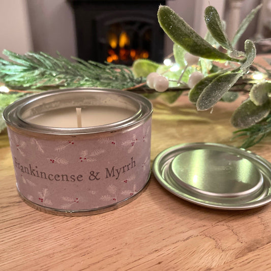 Frankincense and myrrh scented candle in tin holder. Styled on wooden coffee table with a faux garland and fairy lights.
