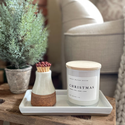 Vegan natural candle with Christmas tree, cinnamon, orange and clove scent. Styled on a ceramic tray with a match holder and a christmas tree in a rustic pot.