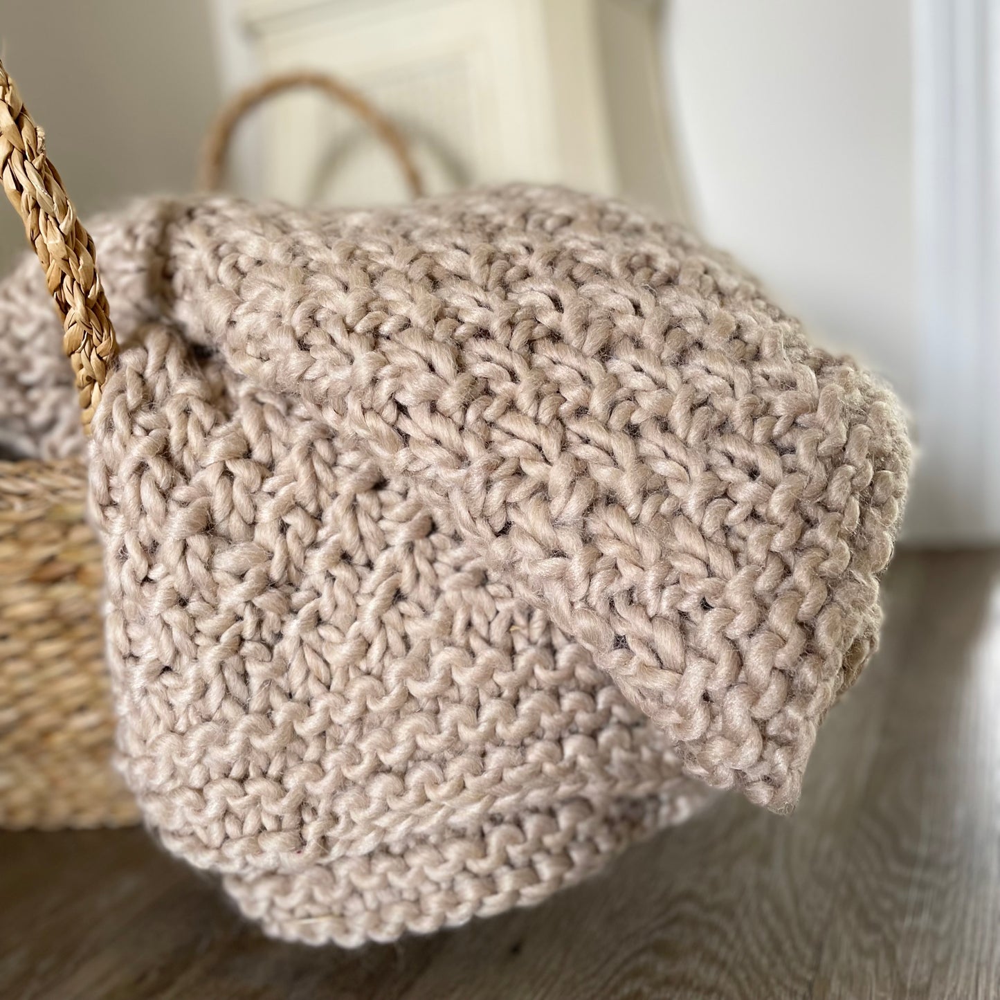 Chunky moss knitted oatmeal throw draped over a rustic wooden armchair in a cosy living room.
