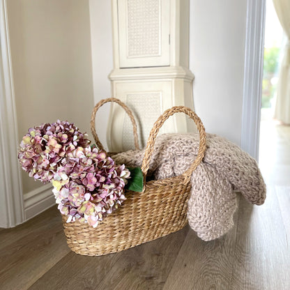 Chunky moss knitted oatmeal throw draped over a rustic seagrass shopper in a cosy hallway.