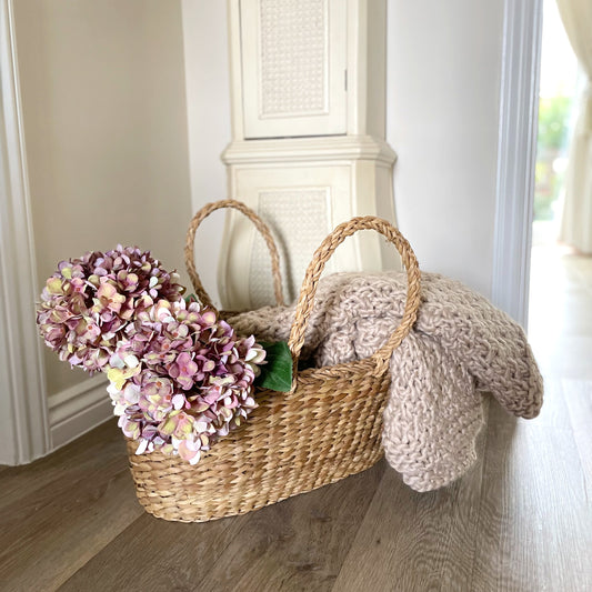 Chunky moss knitted oatmeal throw draped over a rustic seagrass shopper in a cosy hallway.