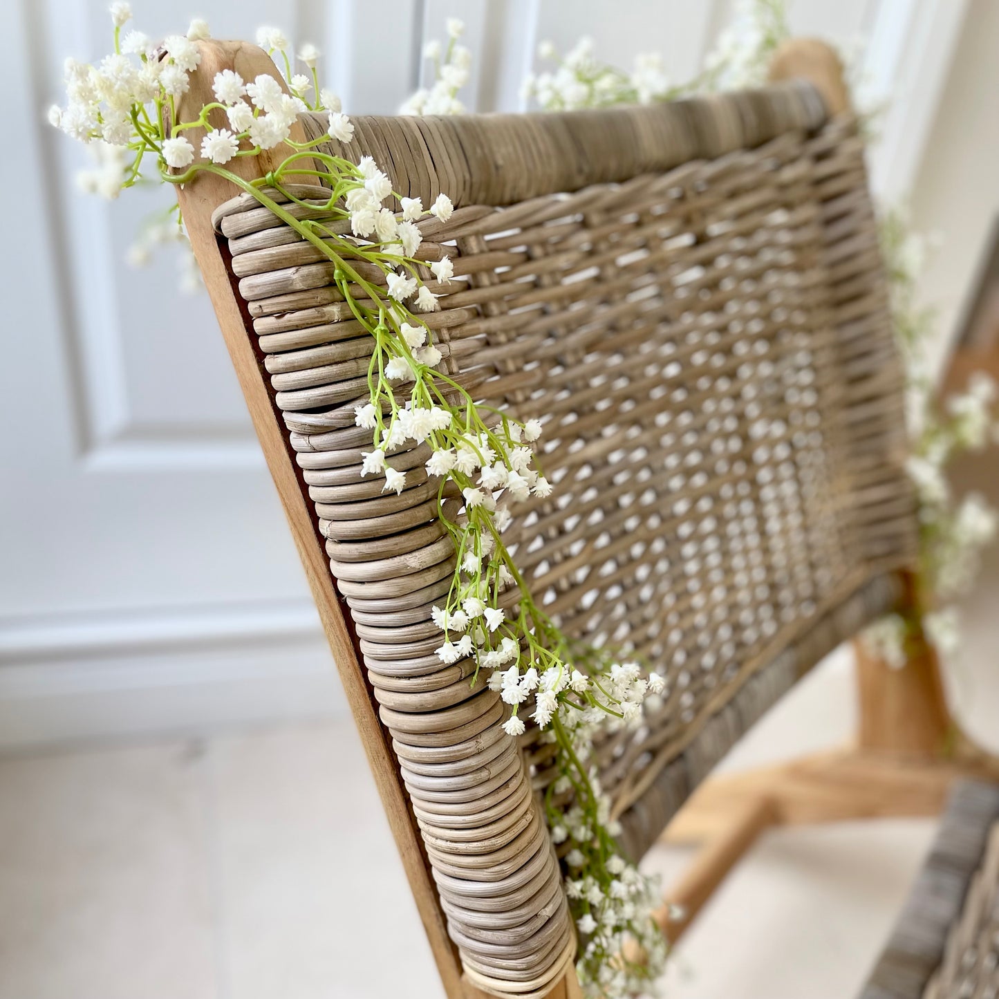White faux gypsophila flower garland draped over a wicker chair.