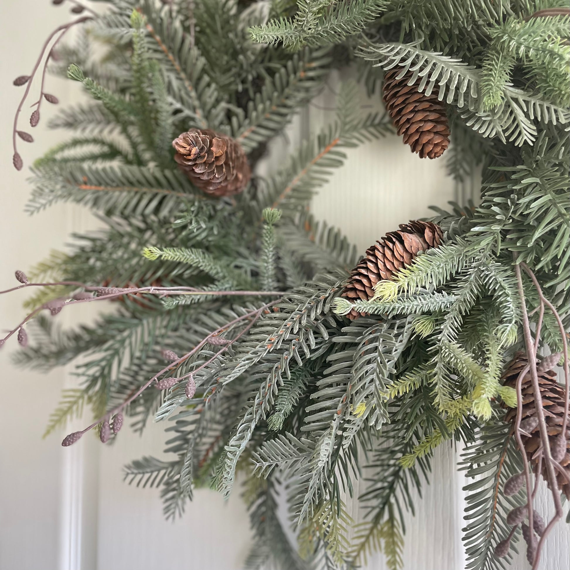 Close up of faux cones and ferns on woodland Christmas wreath. Styled on a white door.
