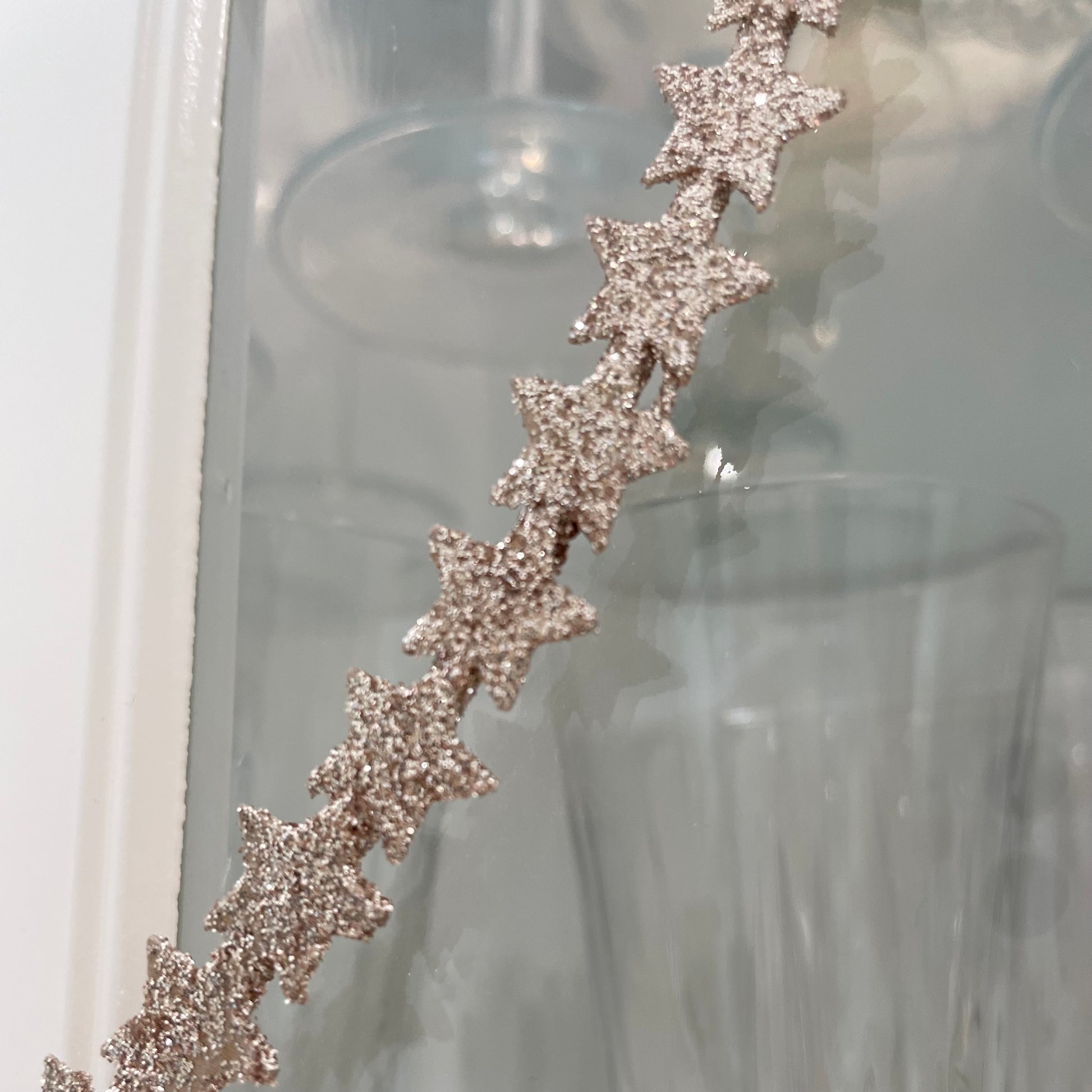 Close up of heart shaped gold glitter star wreath hanging from natural jute string on a glass door.