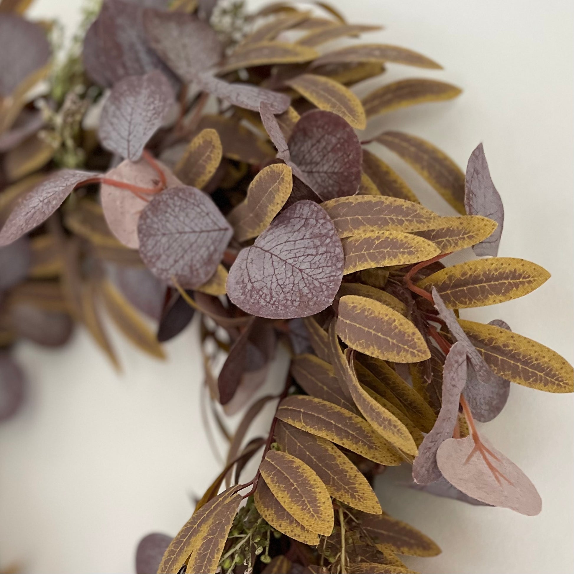 Full autumn foliage wreath with rich fall colours, styled as door or wall decor. Styled on a white wall.