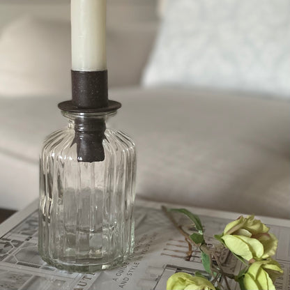 Close up of bottle top candle holder on a bud vase. Styled on a book in a neutral living room.