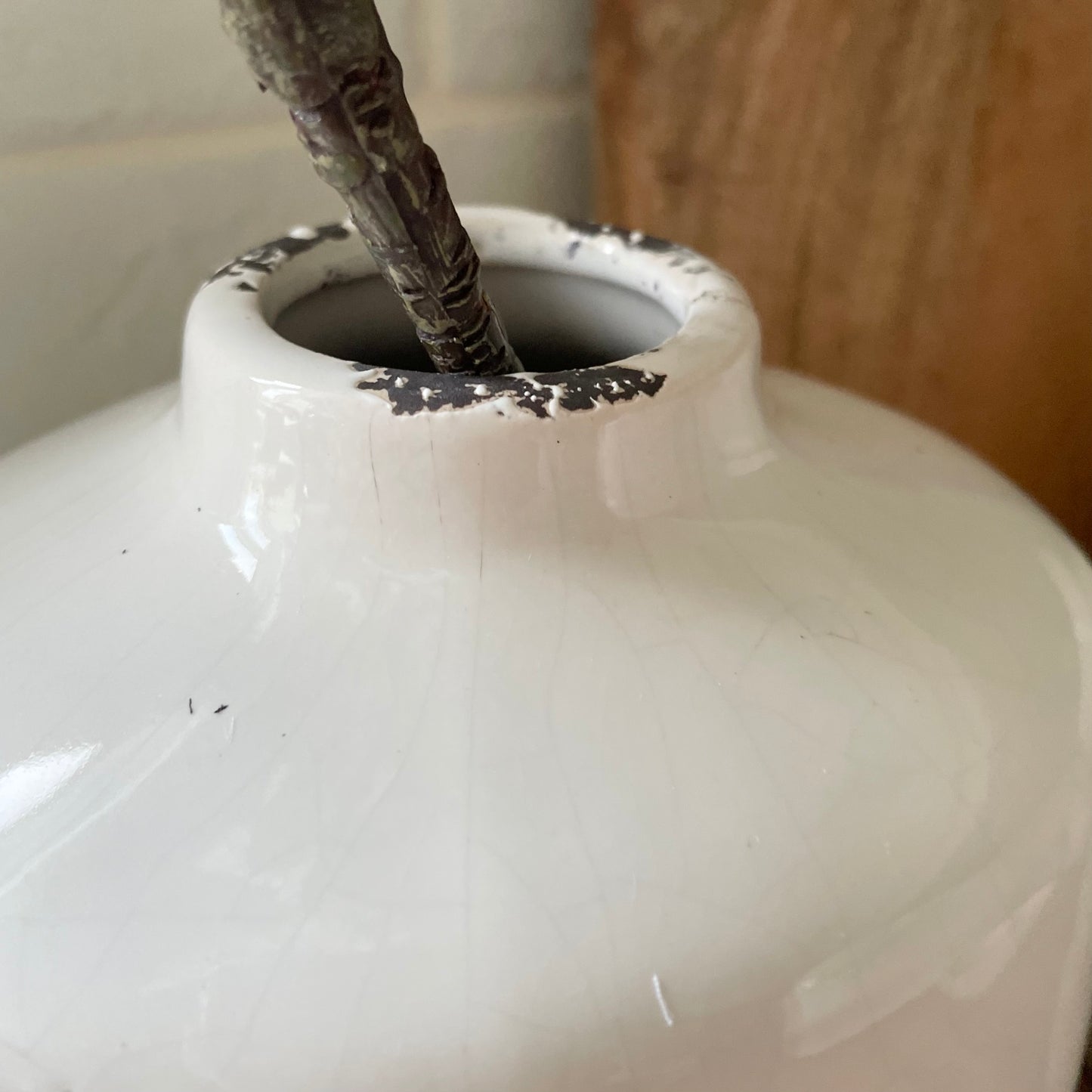 Close up of cream crackle glazed ceramic vase with textured finish, styled with flowers on a rustic table.
