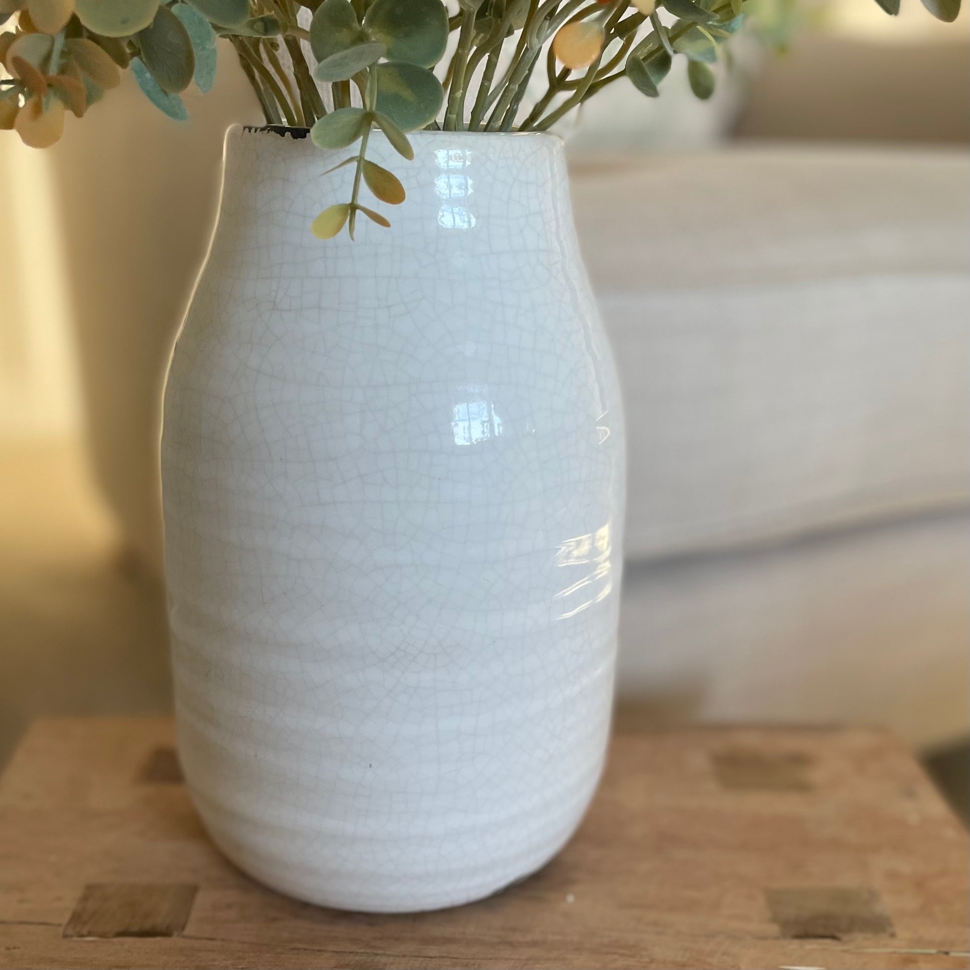 Close up of cream crackle glazed ceramic vase with textured finish. Styled on a wooden stool in a cosy neutral living room.