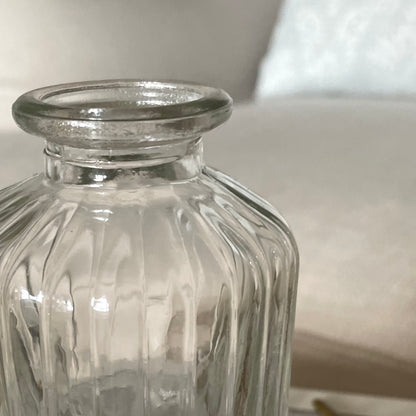 Close up of glass bud vase shown on a neutral background.