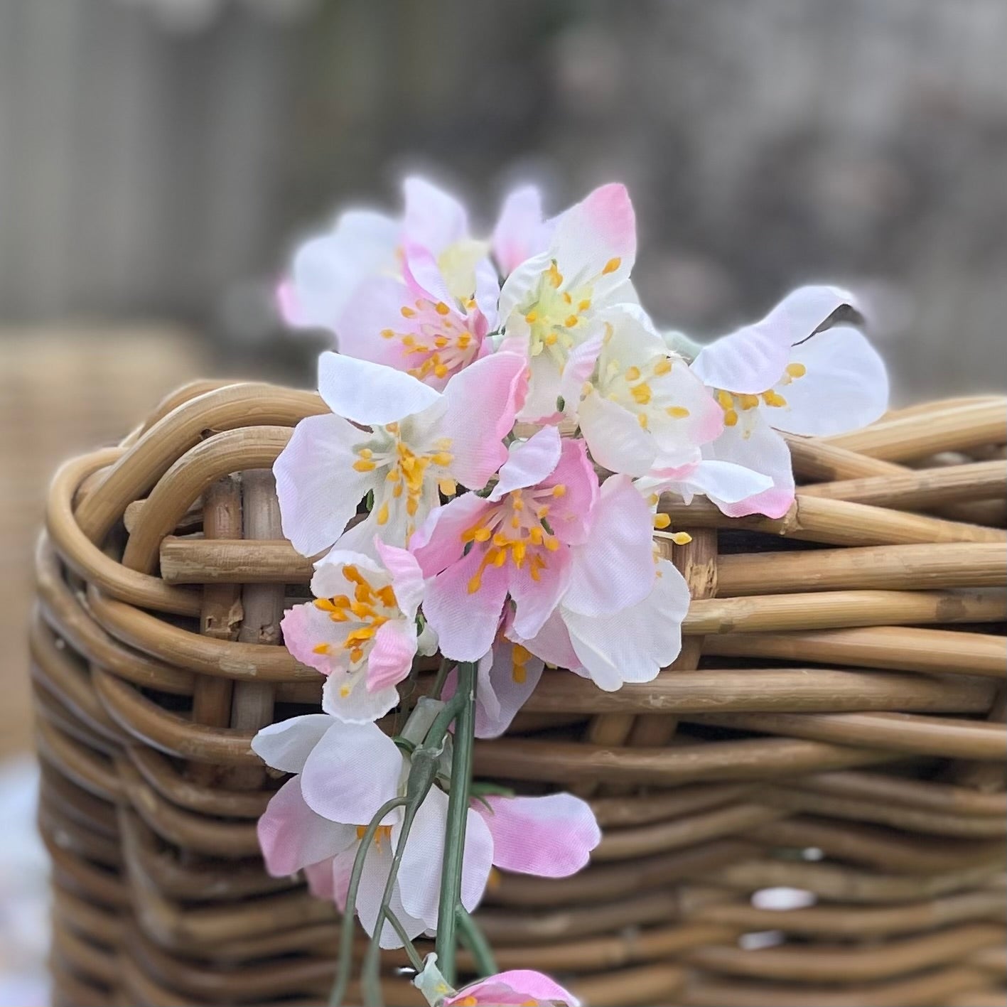 Close up of pink cherry blossom garland with delicate lifelike petals and hanging loops. Draped over a rattan chair in a garden setting.