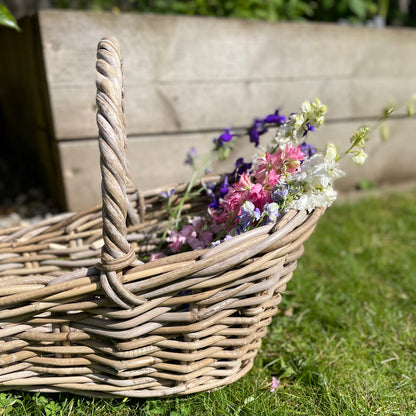 Close up of handwoven rattan flower basket with loop handle, styled with garden flowers.