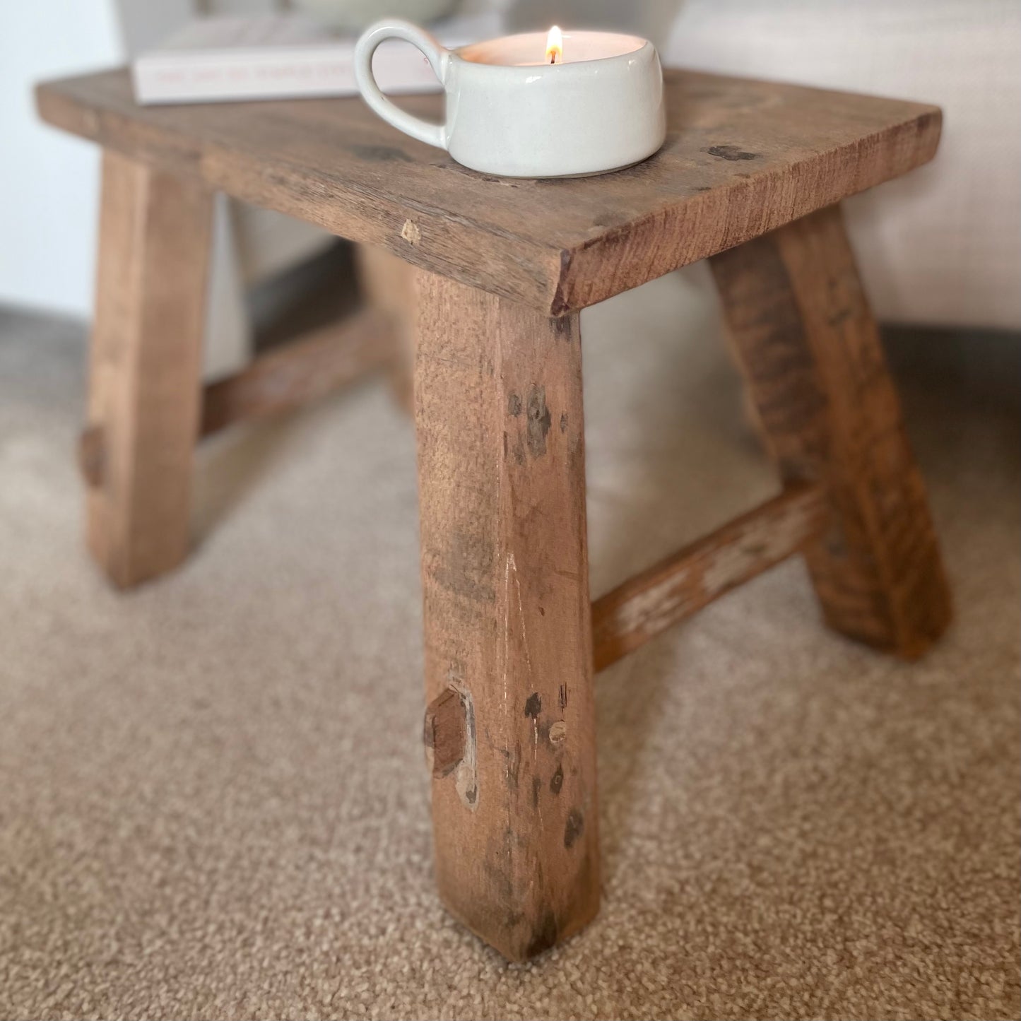 Close up of reclaimed teak wooden display stool with rustic finish styled in a cosy home interior.