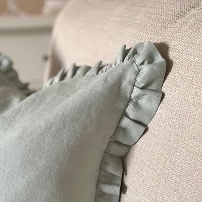 Close up of sage linen cushion with ruffled edge and mother of pearl button detail, styled on a neutral sofa.